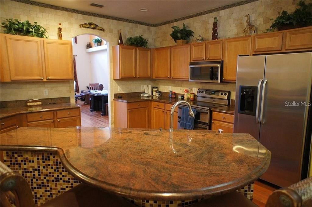 5948 Winchester Isle Road Orlando, FL 32829 - Photo 8 of 23 a kitchen with stainless steel appliances granite countertop a sink a stove top oven a chimney and a refrigerator