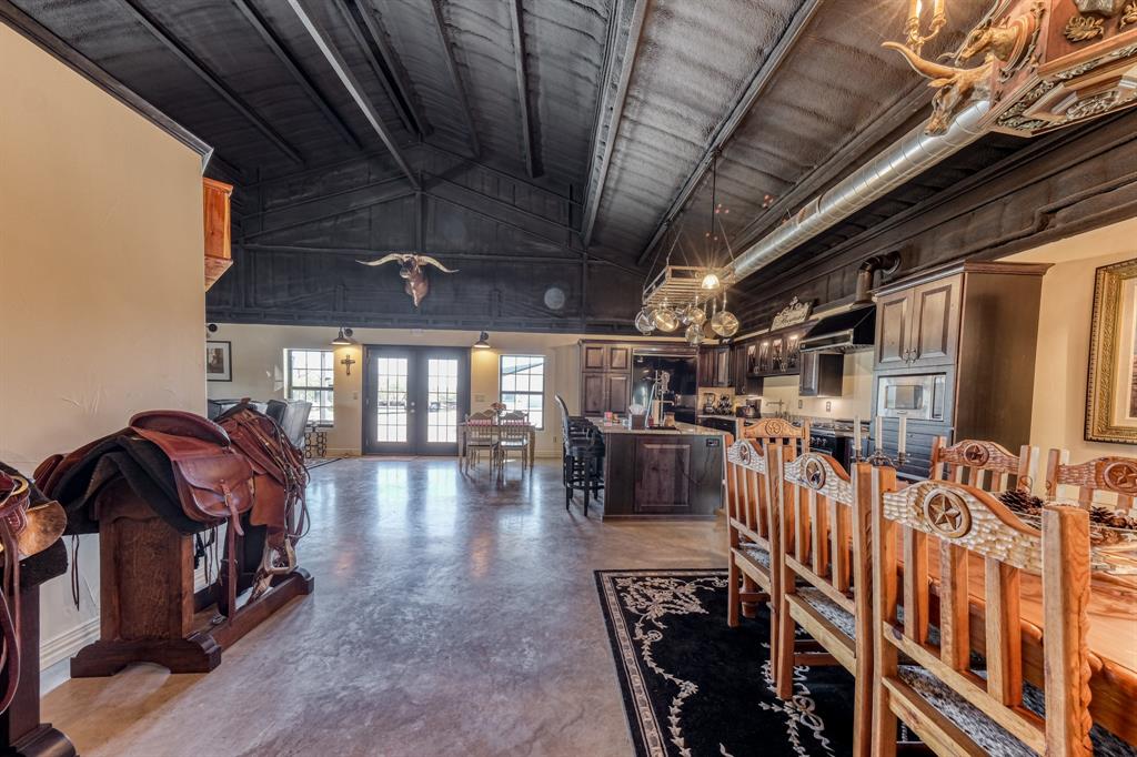 2337 Walsh Road Olney, TX 76374 - Photo 29 of 38 Vaulted ceiling with exposed dark wood beams, polished concrete flooring, kitchen with dark wood cabinetry, kitchen island with seating, and double glass-paneled exterior doors