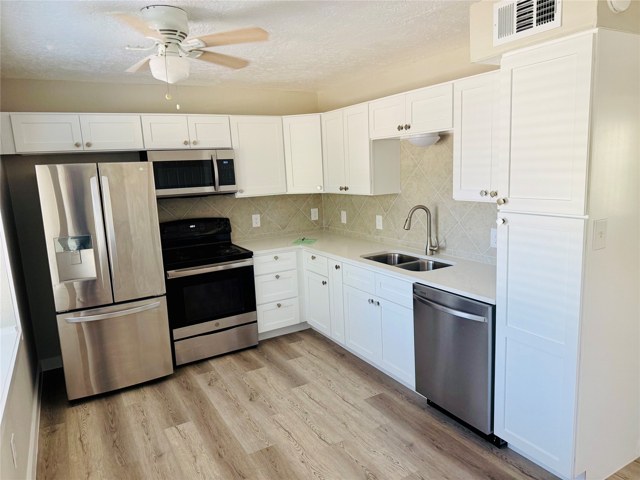 The updated kitchen features white shaker cabinets, quartz countertops, stainless steel appliances, and ample storage.