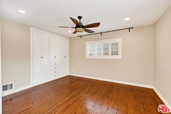 a view of an empty room with wooden floor and a ceiling fan