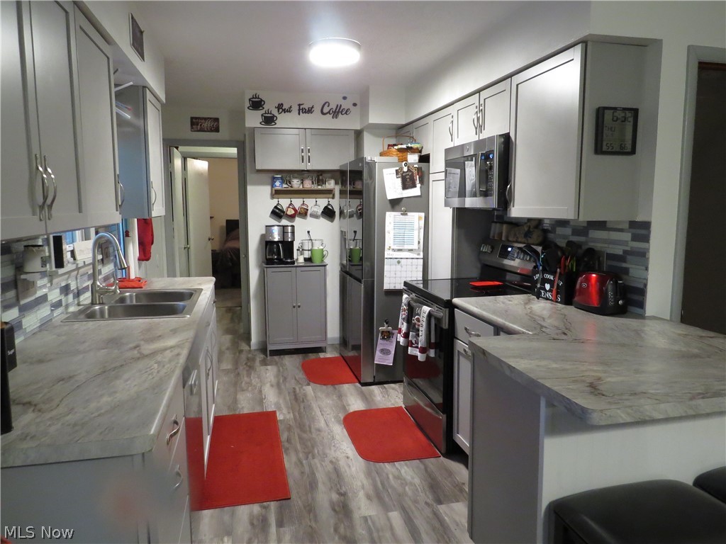 9811 Church Road Huron, OH 44839 - Photo 21 of 28 Kitchen with light hardwood / wood-style flooring, stainless steel appliances, kitchen peninsula, sink, and tasteful backsplash