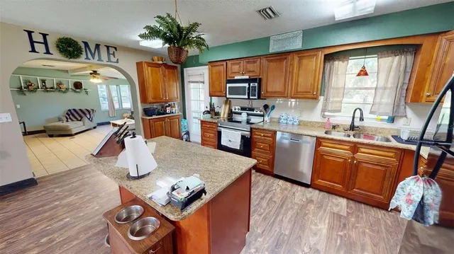a kitchen with stainless steel appliances granite countertop a refrigerator a sink dishwasher a stove and a dining table with wooden floor
