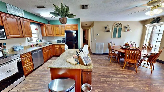 a kitchen with stainless steel appliances granite countertop a sink a stove a dining table and chairs with wooden floor