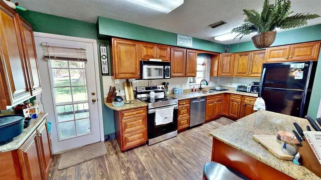 a kitchen with stainless steel appliances granite countertop a refrigerator a sink dishwasher a stove and a dining table with wooden floor