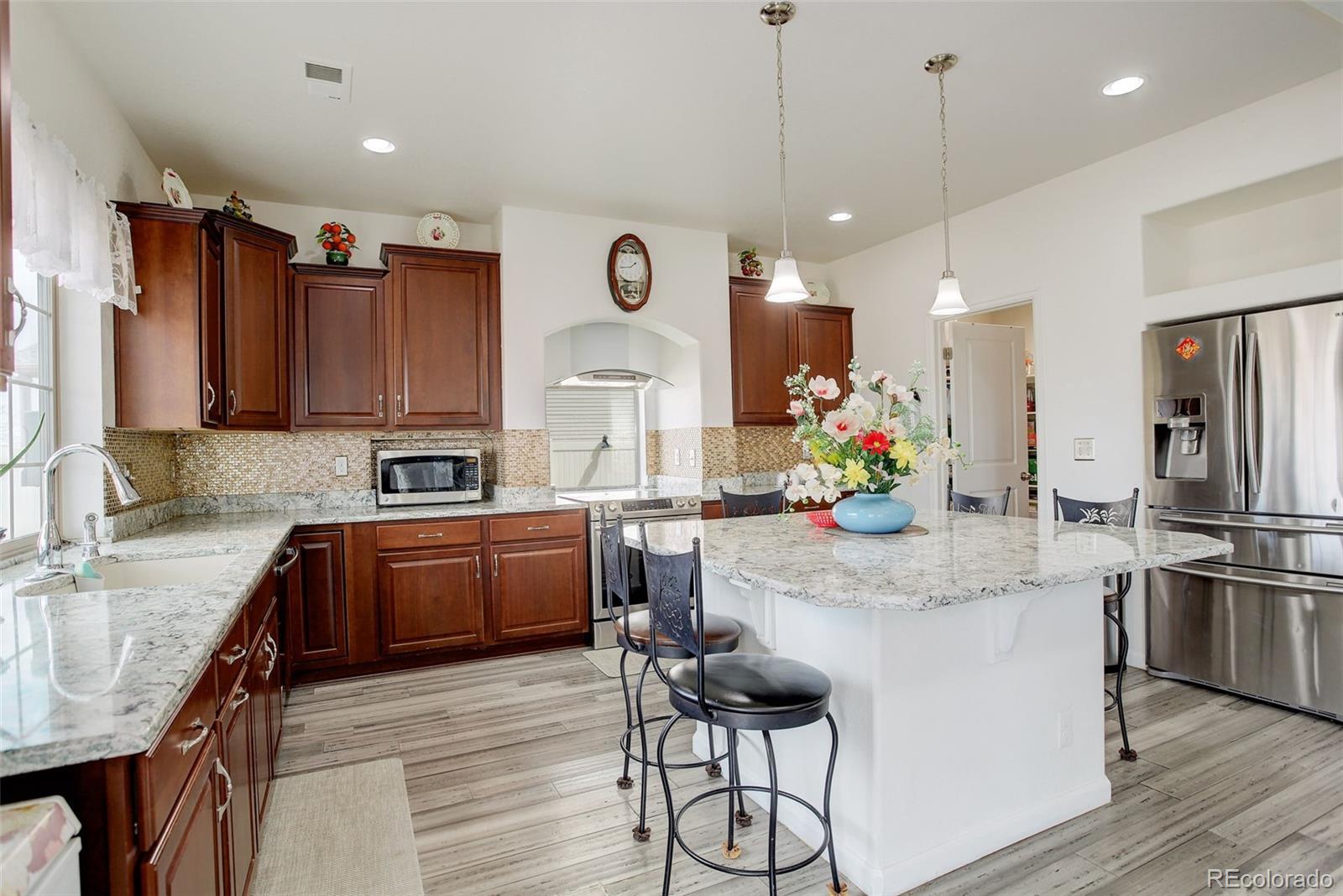 4971 Ceylon Way Denver, CO 80249 - Photo 13 of 40 a kitchen with granite countertop a table chairs refrigerator and microwave