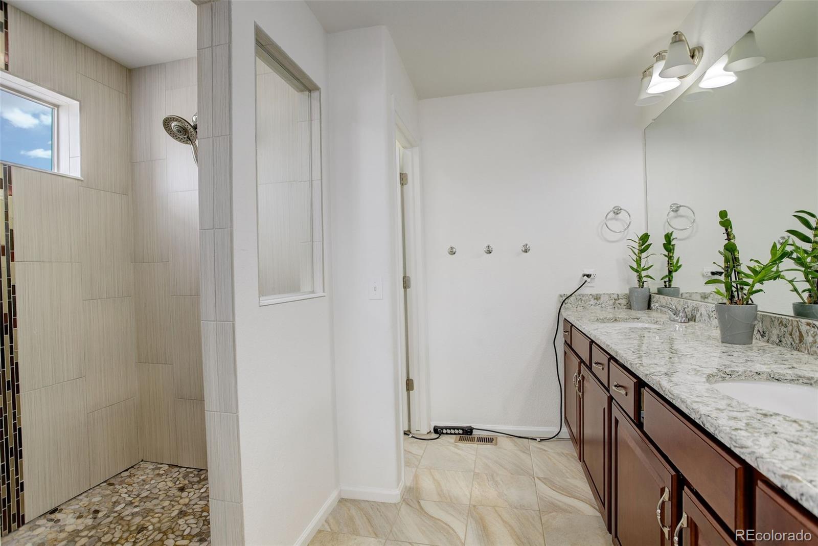 4971 Ceylon Way Denver, CO 80249 - Photo 19 of 40 a bathroom with a granite countertop sink a mirror and a shower