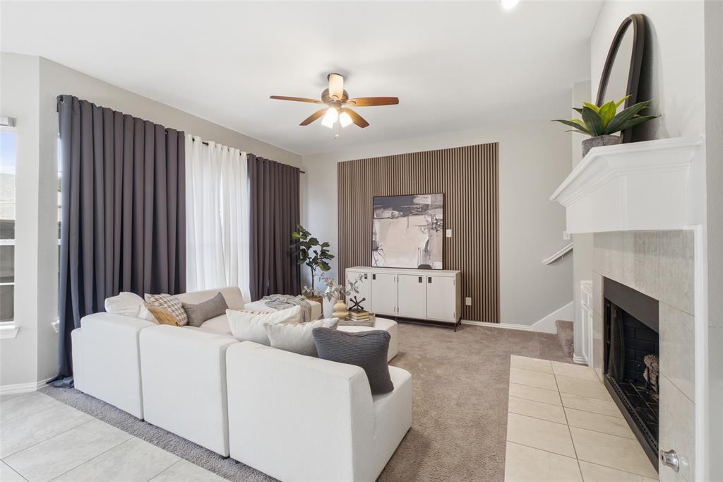 A warm wood slat feature wall adds modern texture and depth to the family room, balanced by the tiled fireplace and white mantel on the opposite side. An oversized ceiling fan and a neutral palette keep the room feeling light and livable.