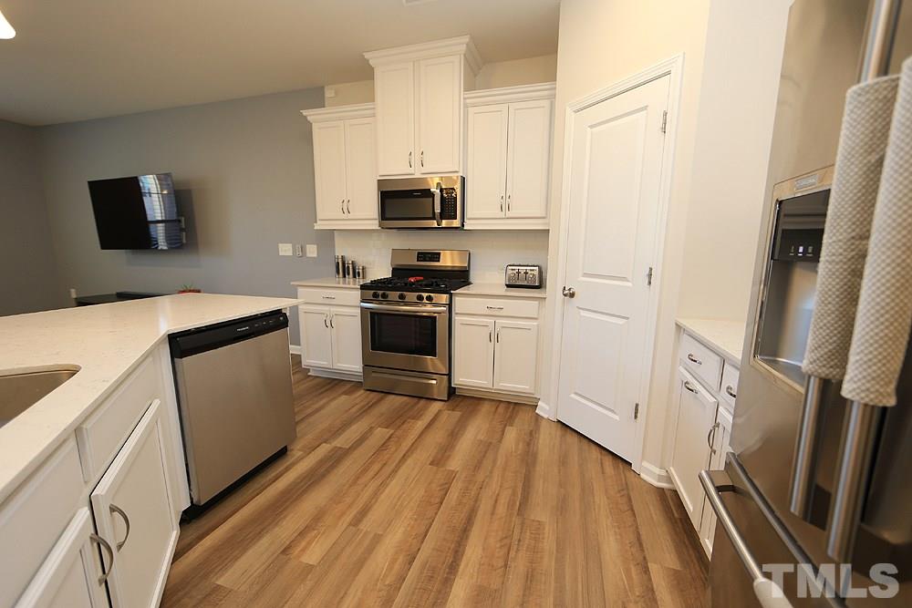 6108 Beale Loop Raleigh, NC 27616 - Photo 3 of 19 a kitchen with stainless steel appliances a stove top oven a sink a refrigerator white cabinets and wooden floor