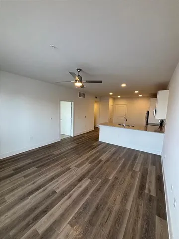 an empty room with wooden floor and kitchen view