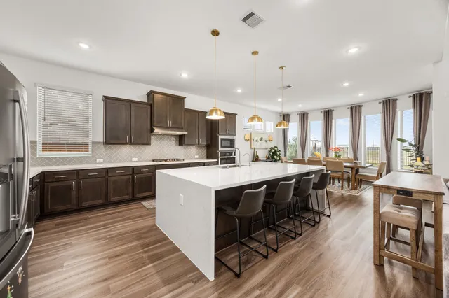 a large kitchen with stainless steel appliances a stove a sink dishwasher and a dining table with wooden floor