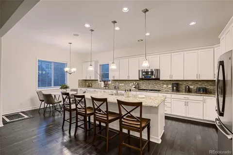 a kitchen with stainless steel appliances granite countertop a stove a sink a refrigerator a dining table and chairs with wooden floor