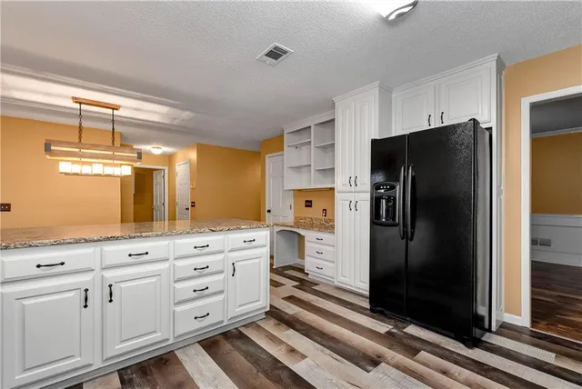 a kitchen with stainless steel appliances granite countertop a refrigerator a sink dishwasher a stove and white cabinets with wooden floor