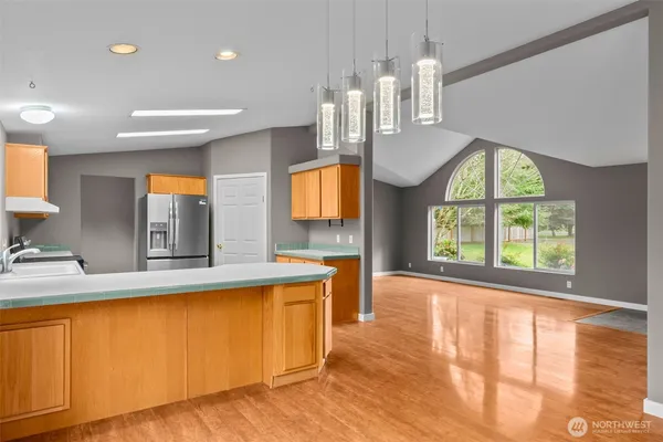 a view of a kitchen with kitchen island a window wooden floor and a view of living room