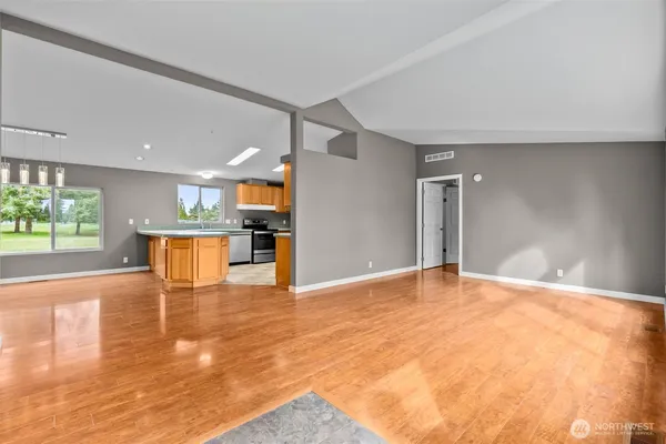 a view of an empty room with wooden floor and a kitchen