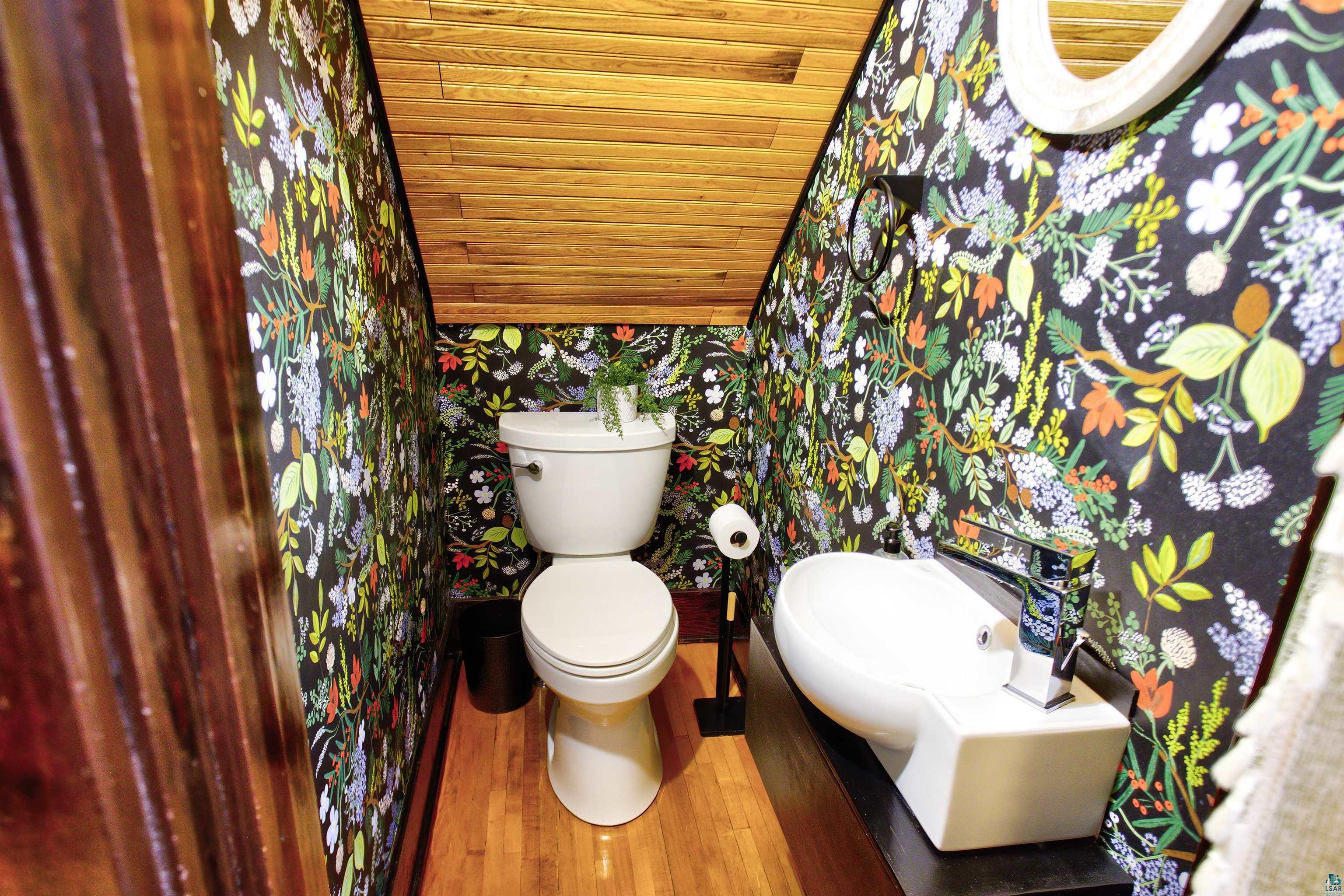 24 East Conan Street Ely, MN 55731 - Photo 22 of 27 Compact powder room featuring botanical print wallpaper, wood-finish flooring, and a natural wood-plank sloped ceiling
