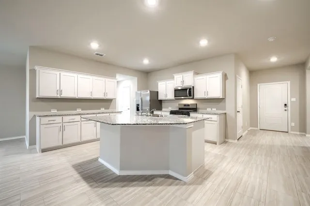 a large kitchen with kitchen island a stove a sink a refrigerator and white cabinets with wooden floor