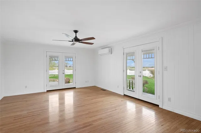 an empty room with wooden floor chandelier fan and windows