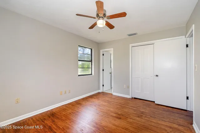 an empty room with wooden floor ceiling fan and window