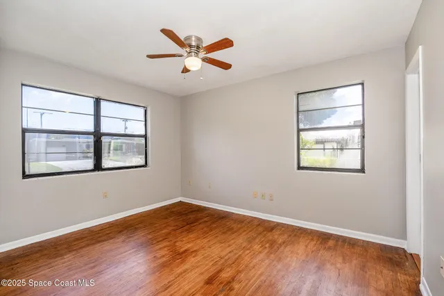 an empty room with wooden floor chandelier and windows