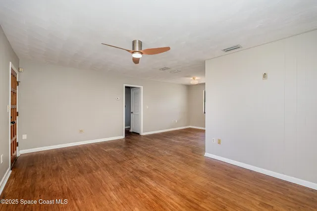a view of an empty room with wooden floor and a ceiling fan