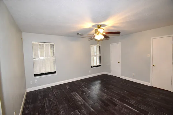 an empty room with wooden floor chandelier fan and windows