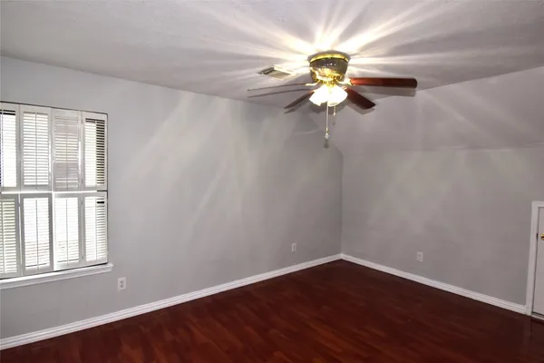 an empty room with wooden floor chandelier fan and windows
