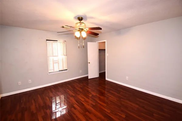 an empty room with wooden floor chandelier fan and windows