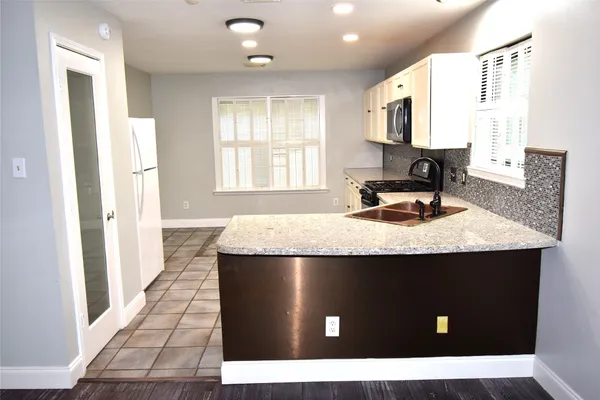 a kitchen with kitchen island granite countertop a refrigerator a sink dishwasher and wooden cabinets with wooden floor