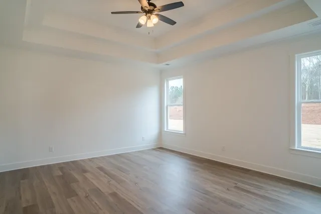 an empty room with wooden floor fan and windows