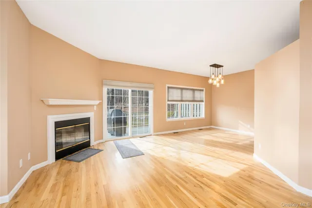 a view of an empty room with wooden floor fireplace and a window