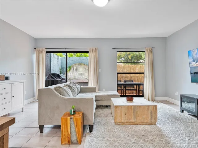 a living room with furniture a rug potted plant and windows
