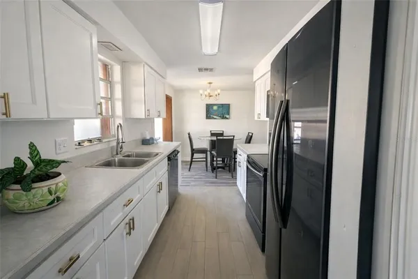 a kitchen with stainless steel appliances granite countertop a refrigerator a sink dishwasher a stove and white cabinets with wooden floor