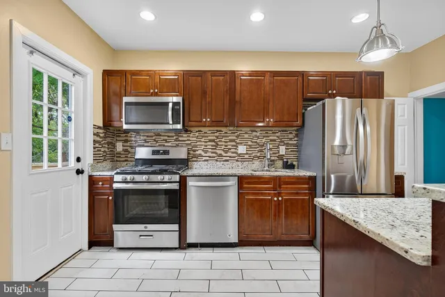 a kitchen with stainless steel appliances granite countertop a refrigerator a stove top oven and a sink