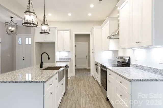 a kitchen with stainless steel appliances granite countertop a sink dishwasher a stove and white cabinets with wooden floor