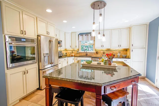 a kitchen with stainless steel appliances granite countertop a refrigerator a stove a sink and white cabinets with wooden floor