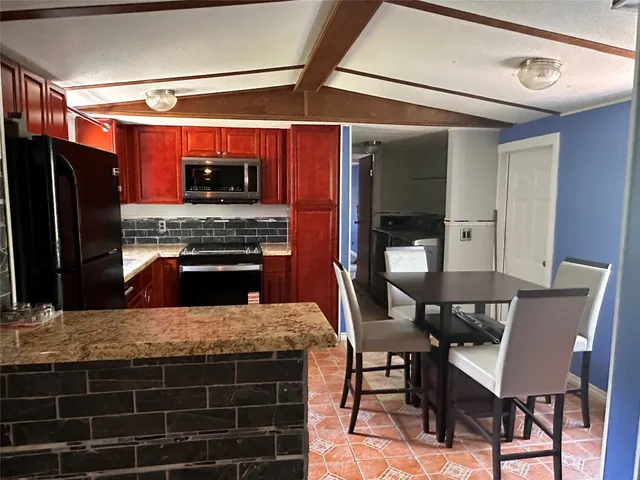 a kitchen with stainless steel appliances kitchen island granite countertop a table chairs and a refrigerator