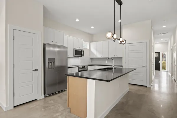 a kitchen with stainless steel appliances granite countertop a refrigerator a sink dishwasher a stove and a dining table with wooden floor