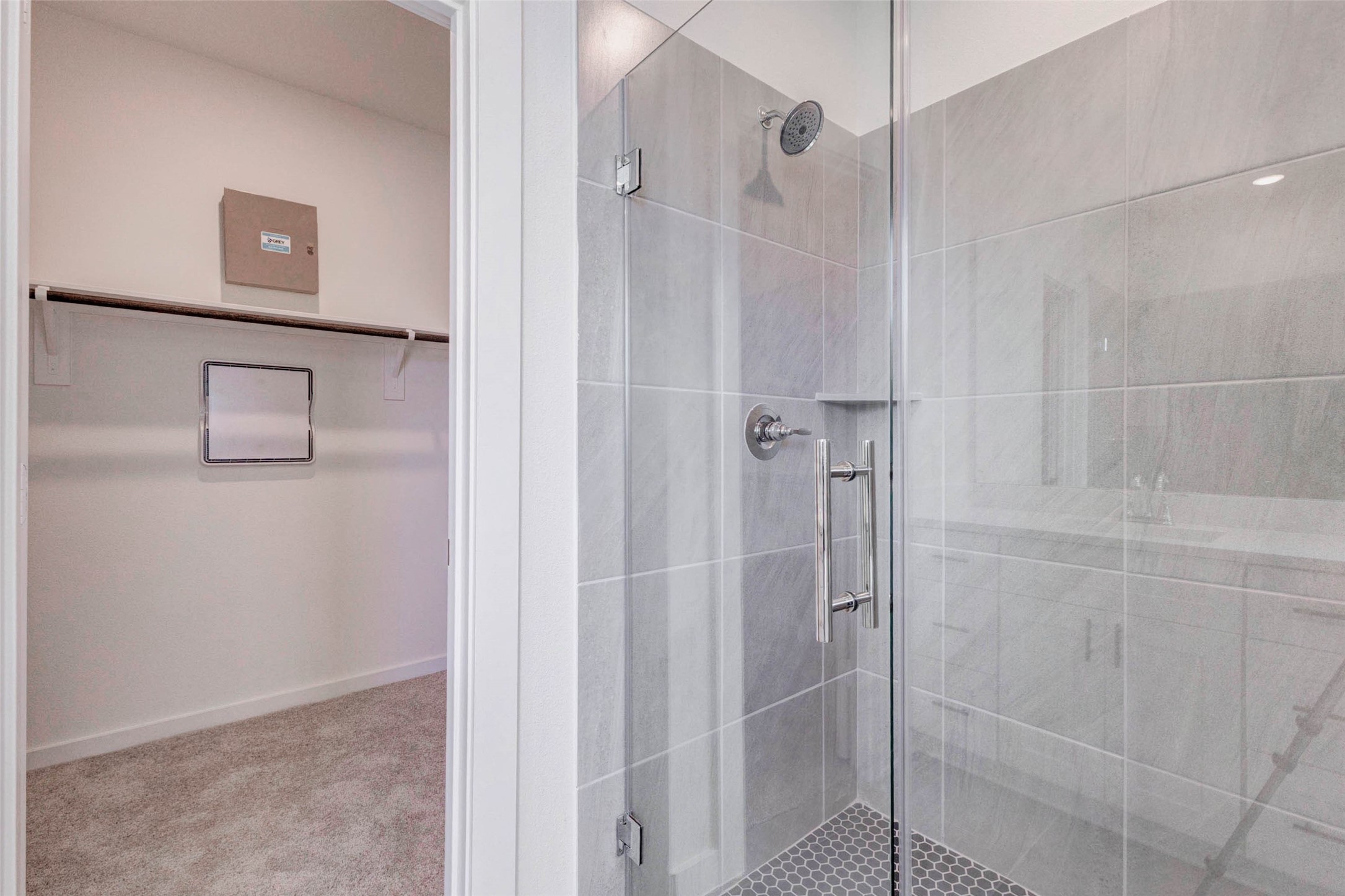 1206 Hemet Court Rosharon, TX 77583 - Photo 13 of 21 Primary shower detail featuring a glass enclosure, gray tile surround, built-in corner shelf, and modern chrome fixtures. The nearby walk-in closet adds everyday convenience, while the neutral tile palette and clean lines give the bath a fresh, spa-like feel designed for comfort, function, and easy maintenance.