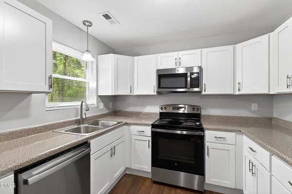 a kitchen with granite countertop white cabinets appliances and a window