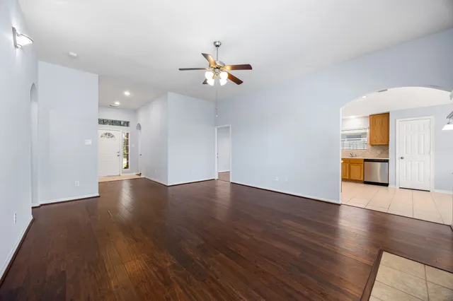 a view of a room with wooden floor a ceiling fan and kitchen view