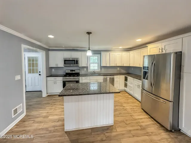 a large kitchen with granite countertop a refrigerator oven a sink dishwasher and white cabinets with wooden floor