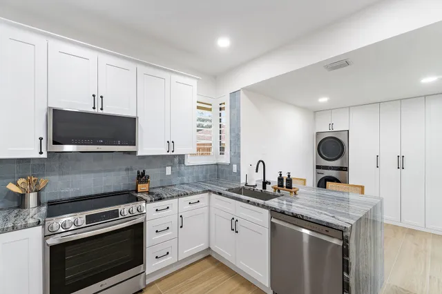 a kitchen with stainless steel appliances granite countertop a stove a sink dishwasher a refrigerator and white cabinets with wooden floor