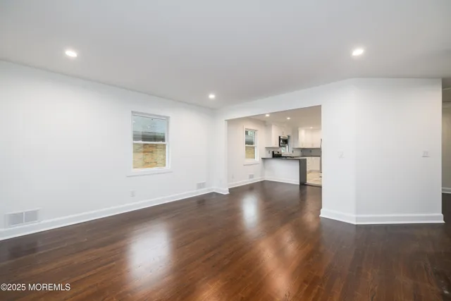 a view of a kitchen and an empty room with wooden floor and a window