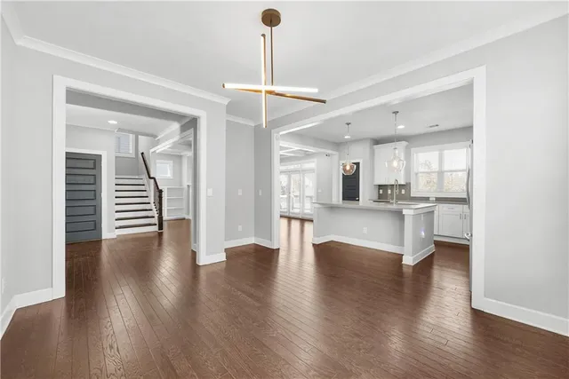 a view of an empty room and kitchen with wooden floor
