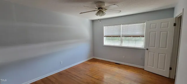 a view of empty room with wooden floor and fan