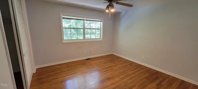 an empty room with wooden floor fan and windows