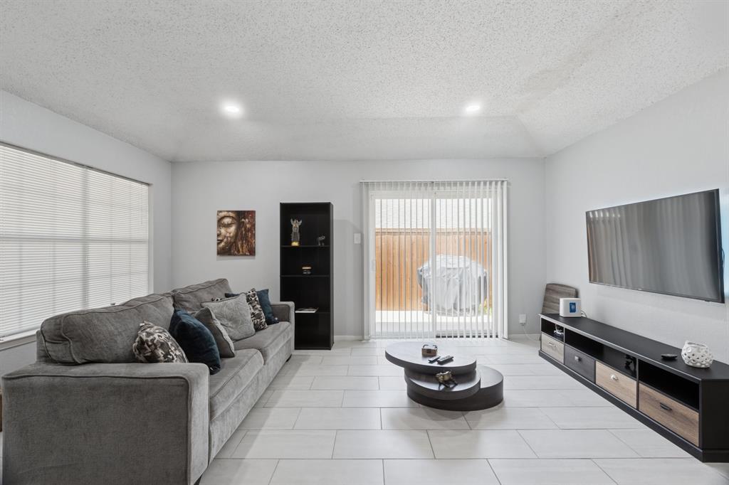 9780 Windy Ridge Road Frisco, TX 75033 - Photo 3 of 25 Spacious living area featuring a vaulted ceiling with recessed lighting, large windows with blinds, light-toned tile flooring, and sliding glass doors with vertical blinds