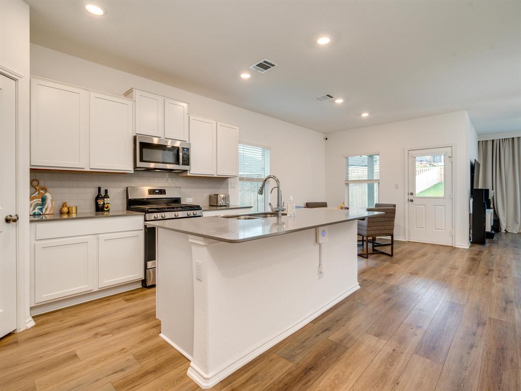 1208 Sweetspire Street Leander, TX 78641 - Photo 1 of 36 Open-concept kitchen with white shaker cabinetry, stainless steel appliances, a light-toned backsplash, and wood-finish flooring