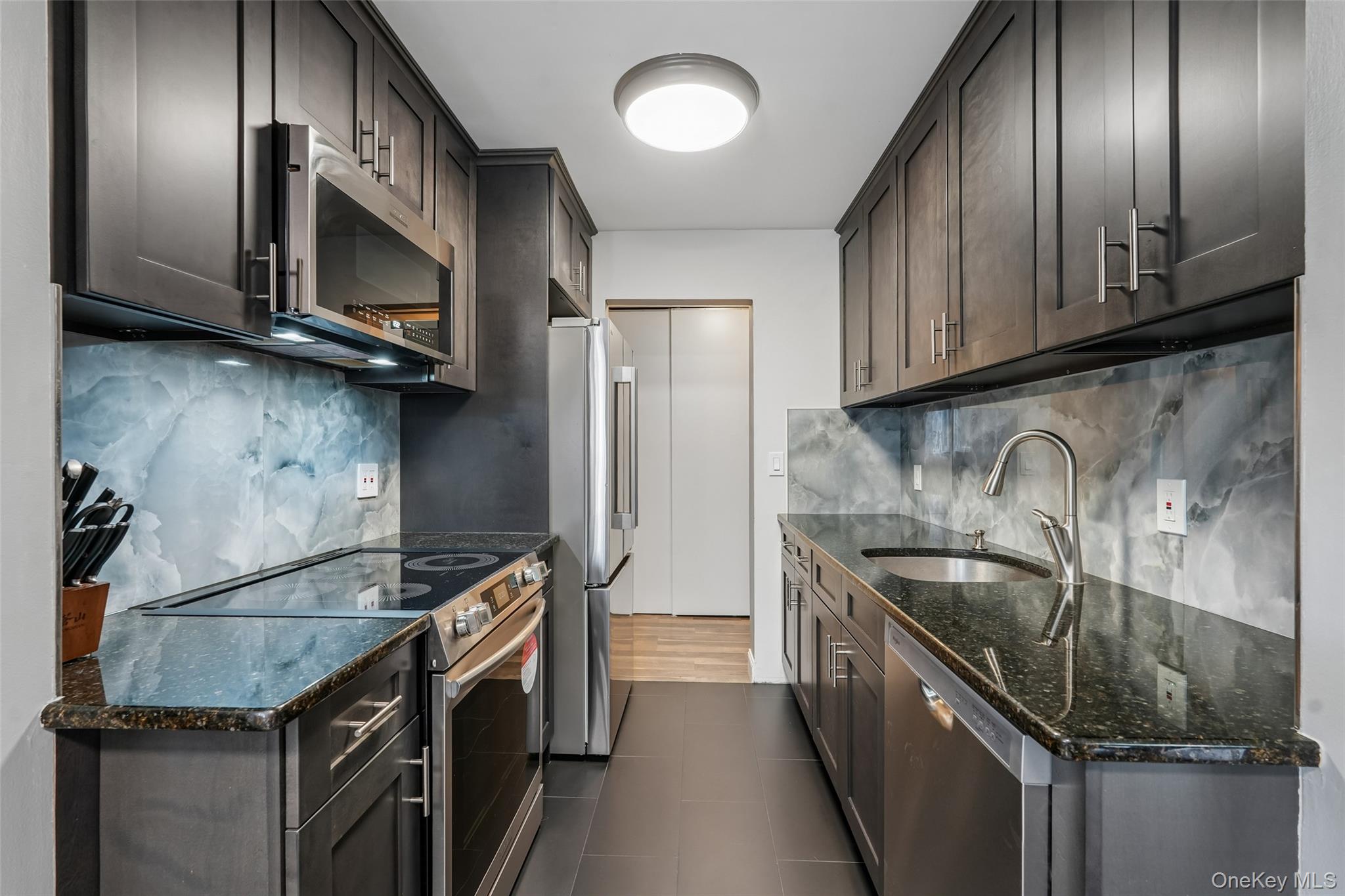 2 Secora Road, Unit C5 Monsey, NY 10952 - Photo 20 of 32 Galley kitchen featuring dark wood-finish cabinetry, stainless steel appliances, granite countertops, and a full-height decorative backsplash
