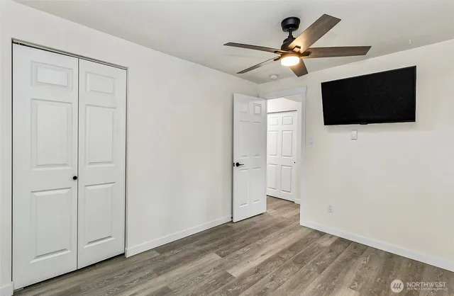a view of an empty room with wooden floor and a ceiling fan